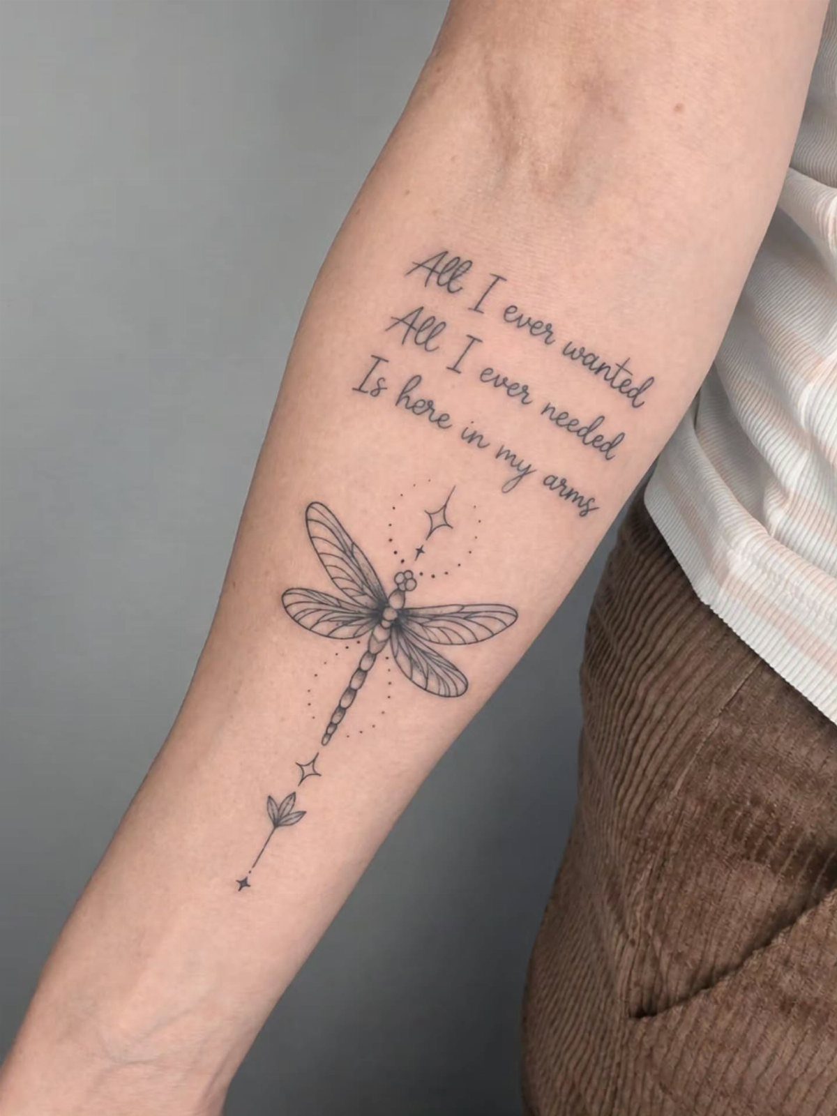 Dragonfly tattoo and cursive quote on a person's forearm with small star accents.