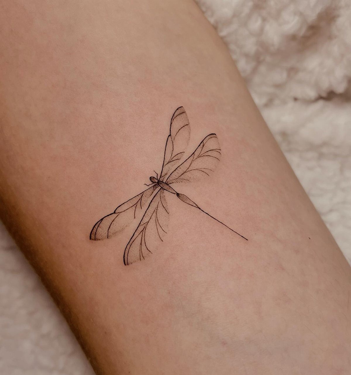 Fine line black ink dragonfly tattoo on a person's forearm
