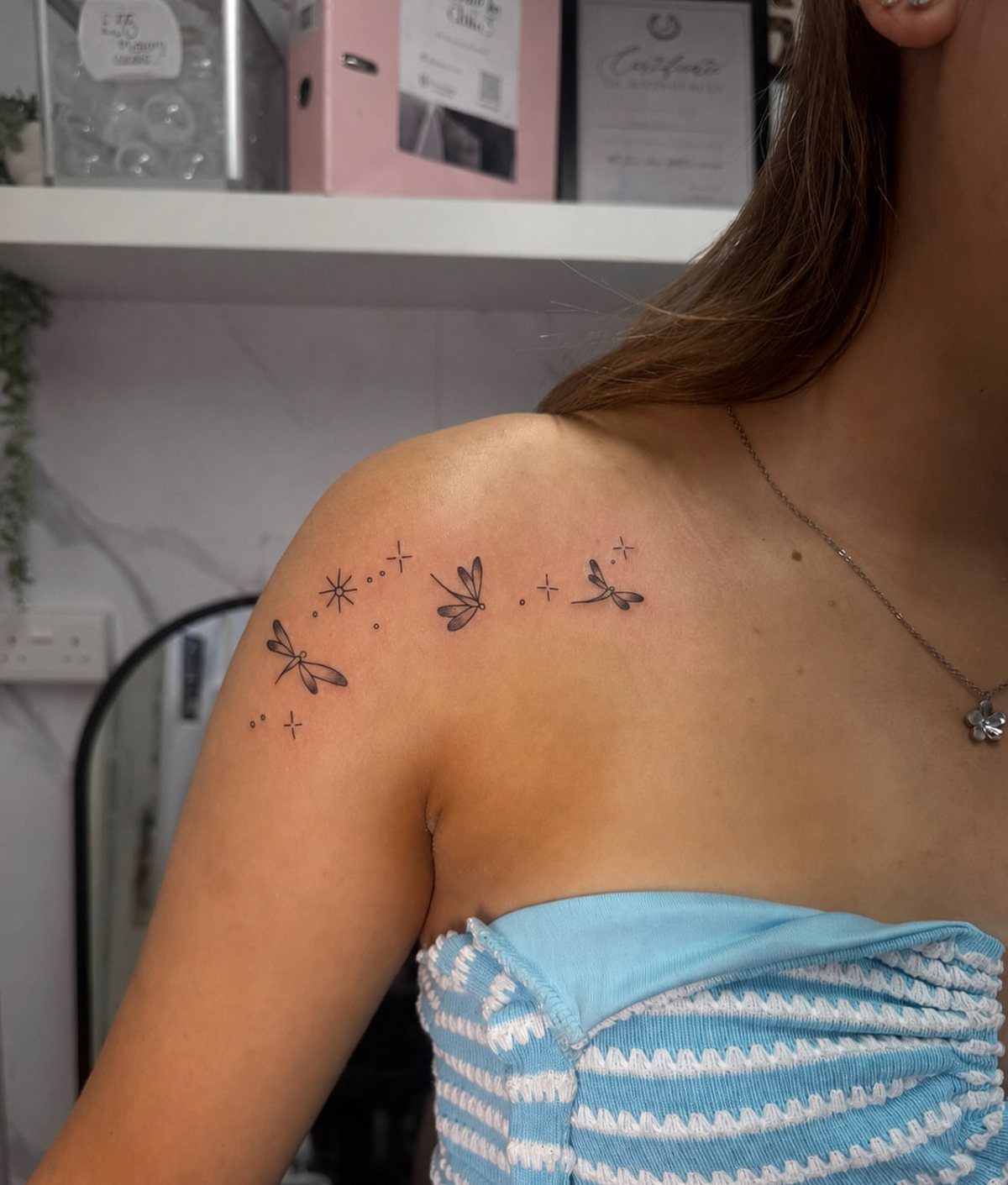 Three small dragonfly tattoos with tiny stars on a person's shoulder and collarbone.