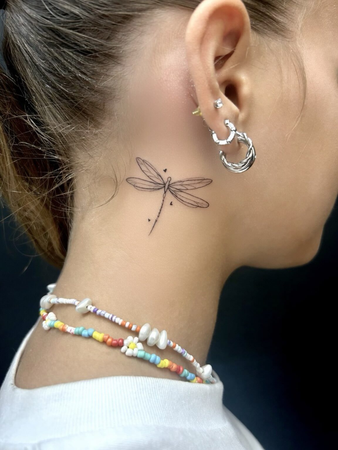 Small black ink dragonfly tattoo on the side of a person's neck