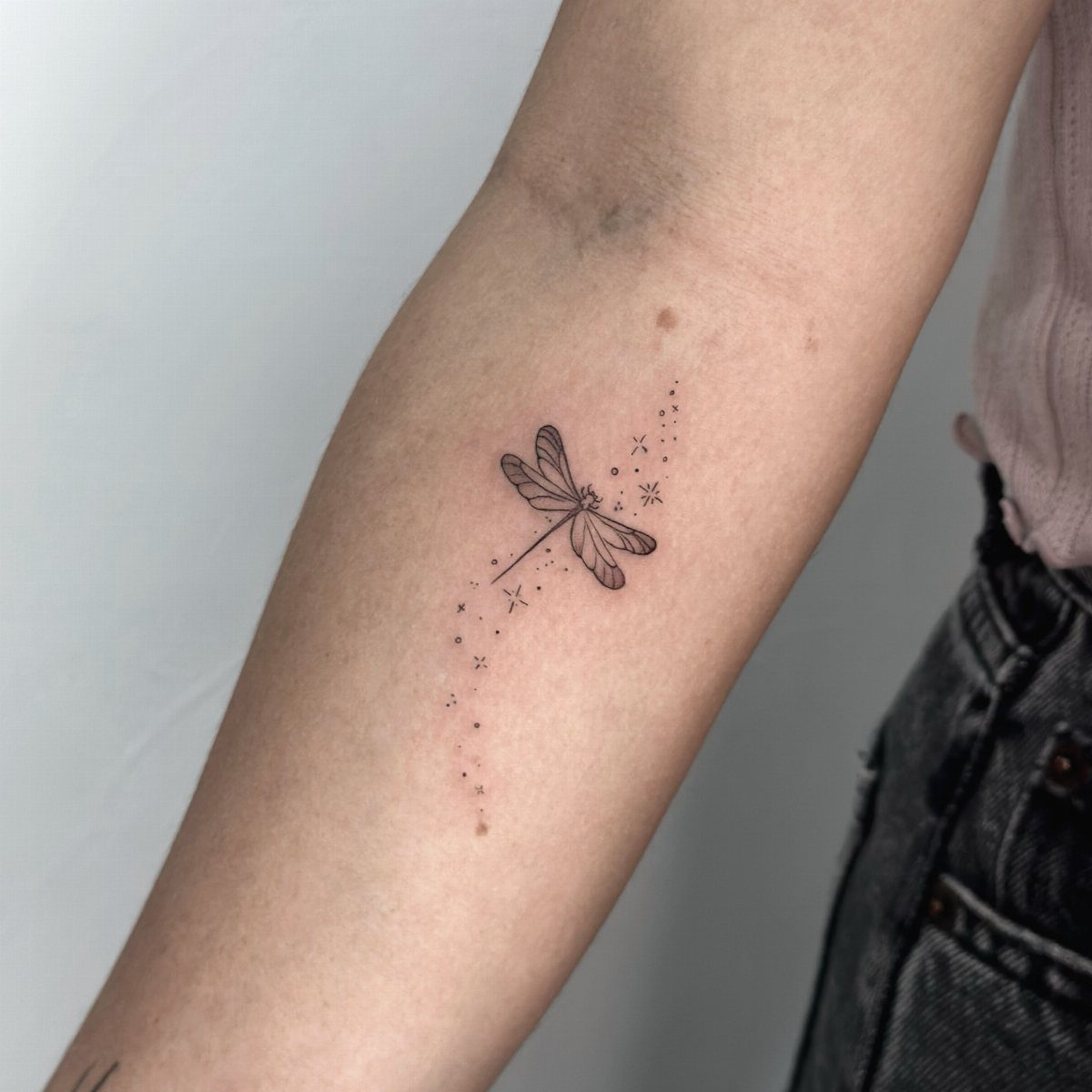 Small black ink dragonfly tattoo with sparkles on a person's forearm