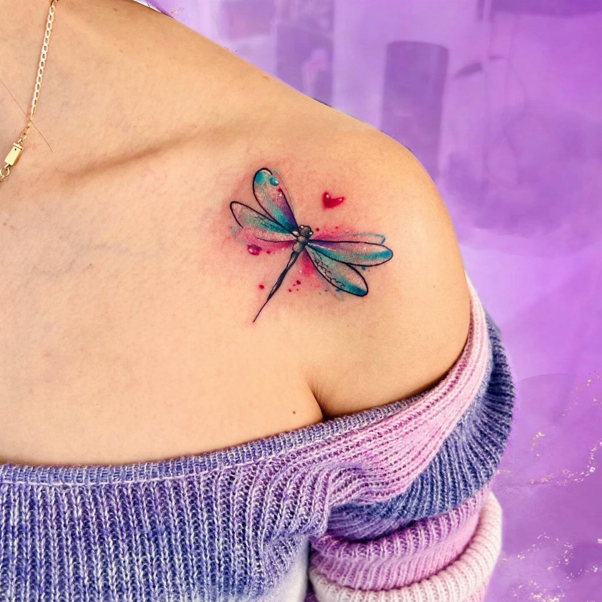 Watercolor dragonfly tattoo in blue and pink on a person's collarbone and shoulder.