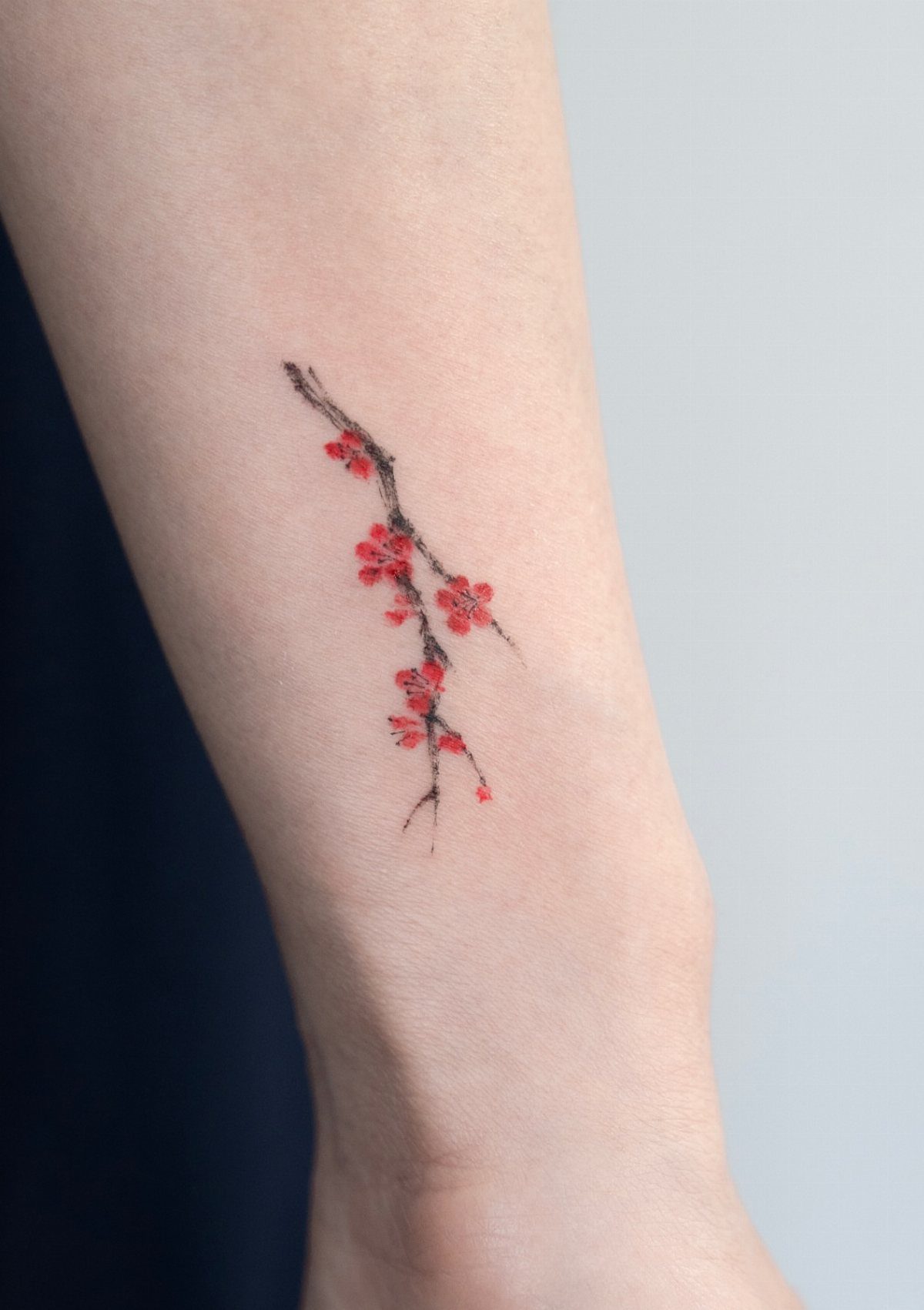 Small tattoo of a dark branch with red blossoms on a person's forearm.