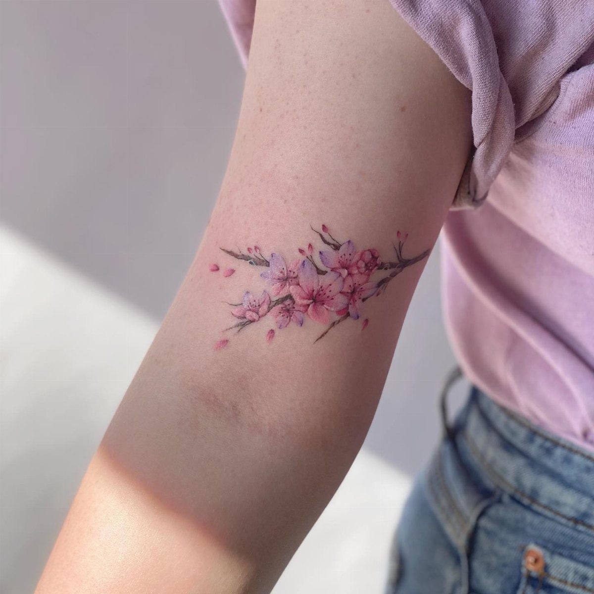 Pink blossom tattoo on a person's upper arm with a brown branch.