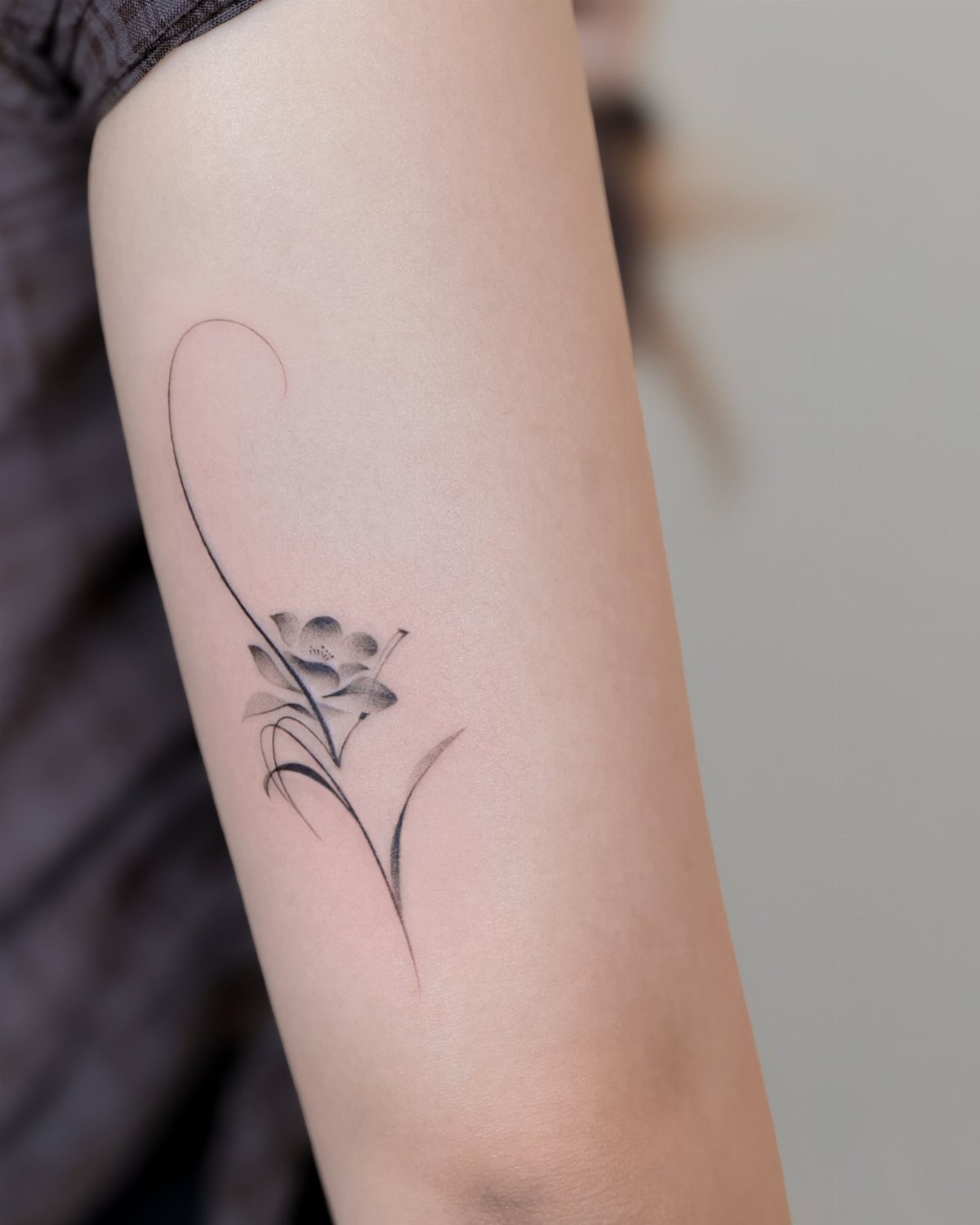 Small black ink flower tattoo with a curved stem on a person's arm.