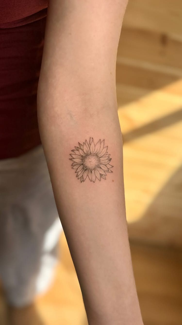 Small sunflower tattoo on a person's inner forearm in black ink.