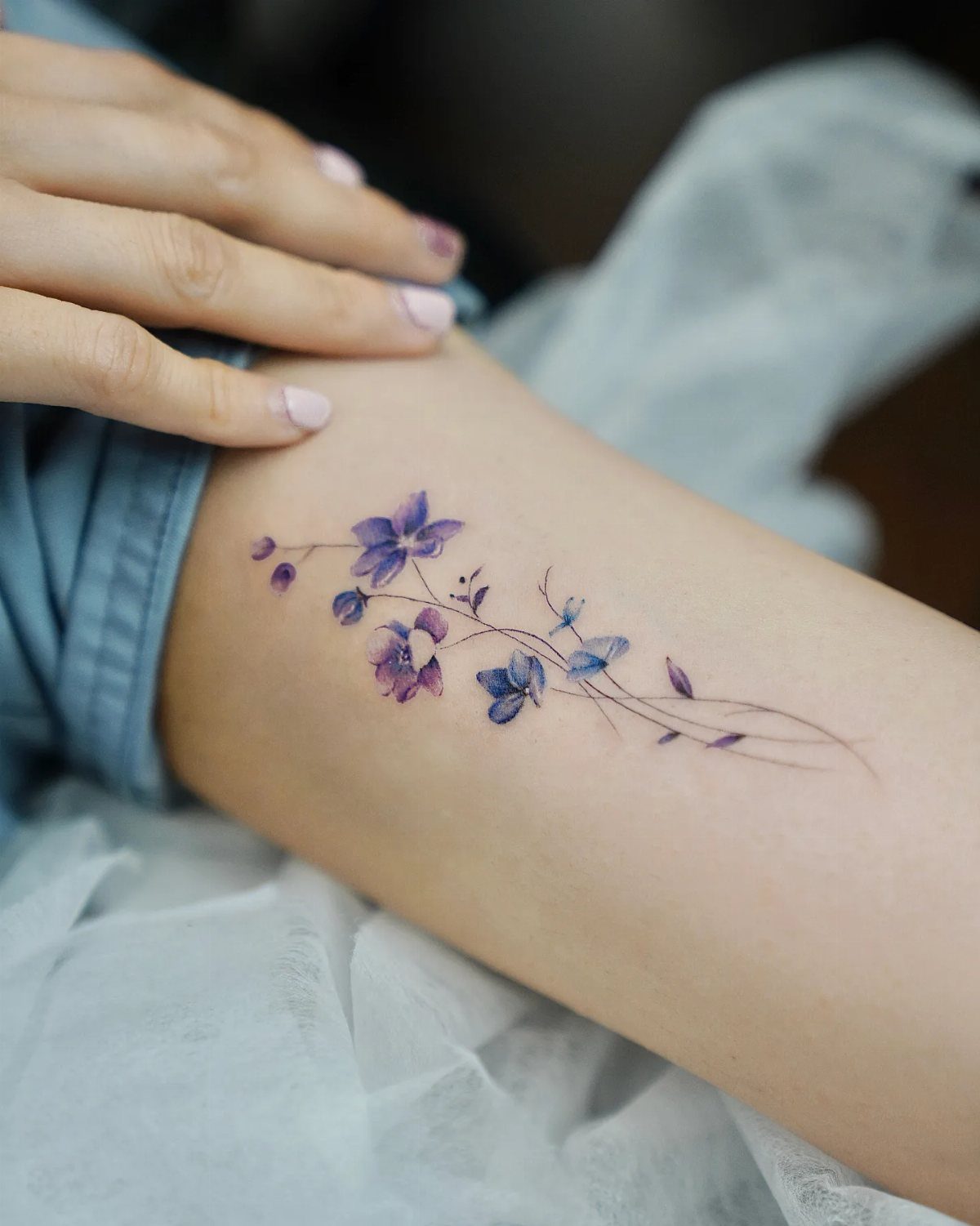 Purple flower tattoo on a person's leg with delicate stems and petals.