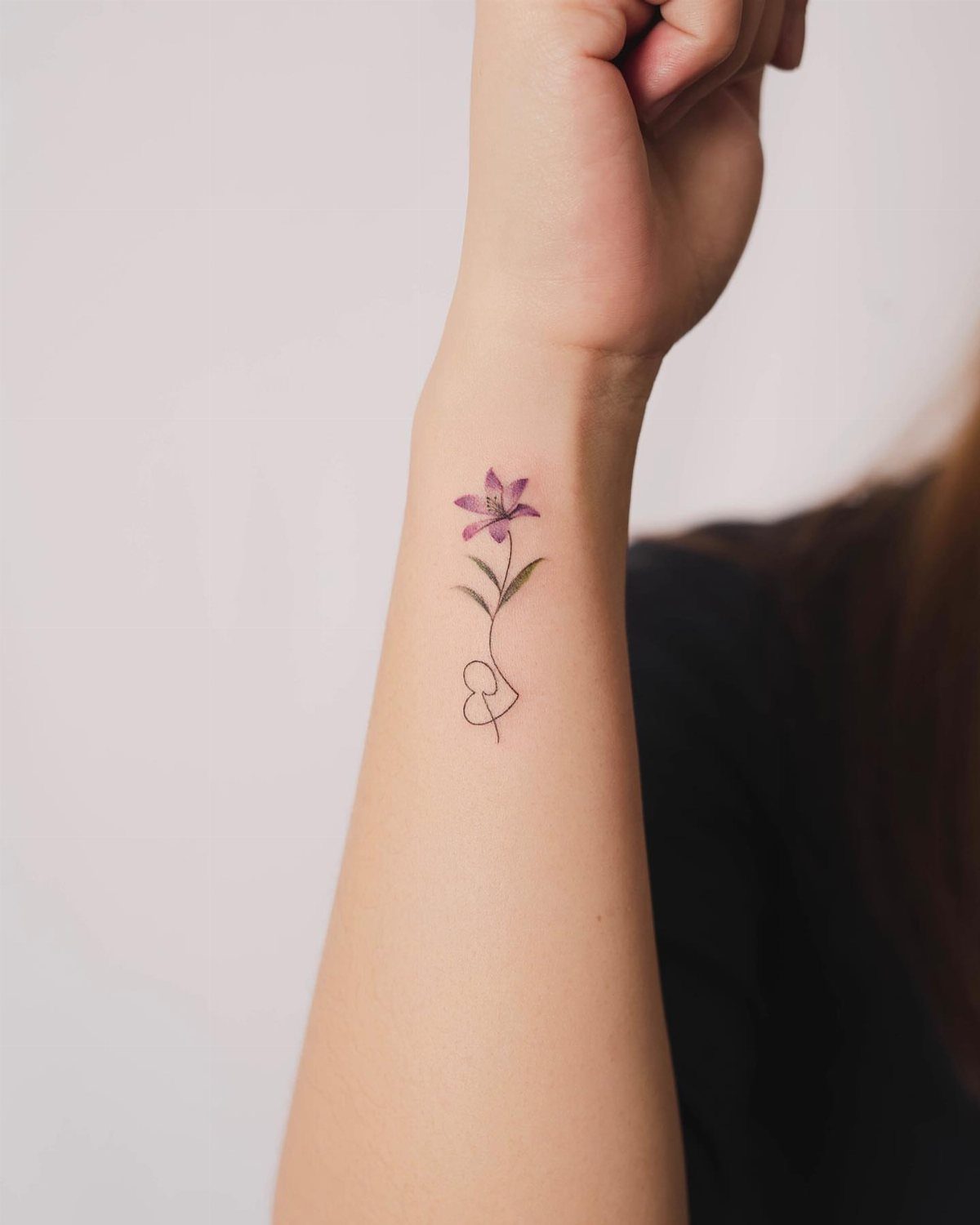 Purple lily flower tattoo with a heart stem on a person's forearm