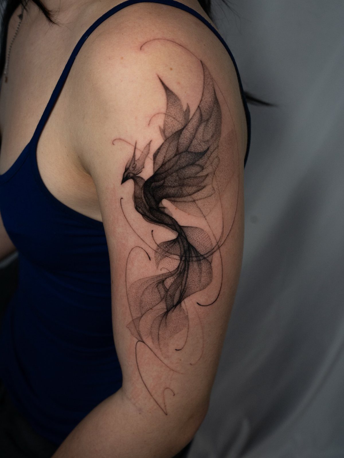 Abstract phoenix tattoo with flowing black lines on a person's upper arm