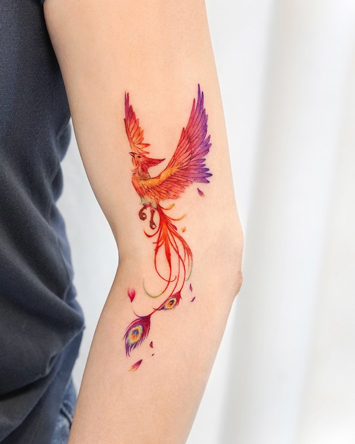 Colorful phoenix tattoo on a forearm with vibrant red, orange, and purple feathers.