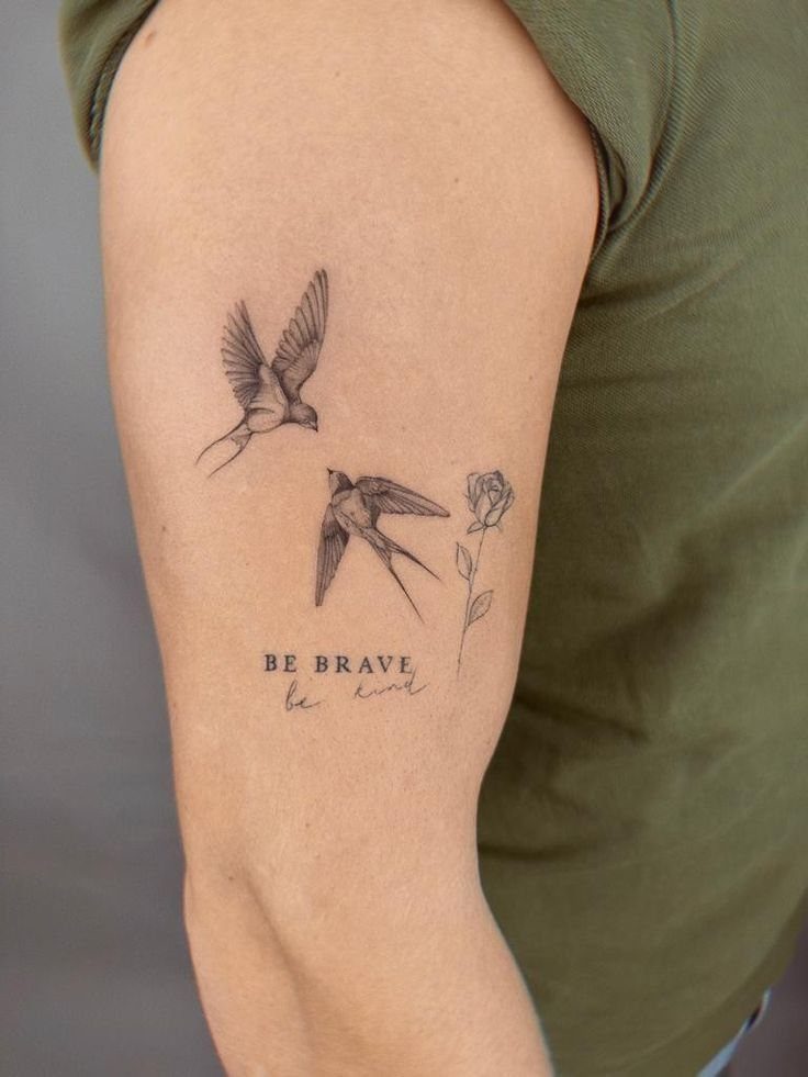 Tattoo of two swallow birds, a rose, and the words Be Brave on arm