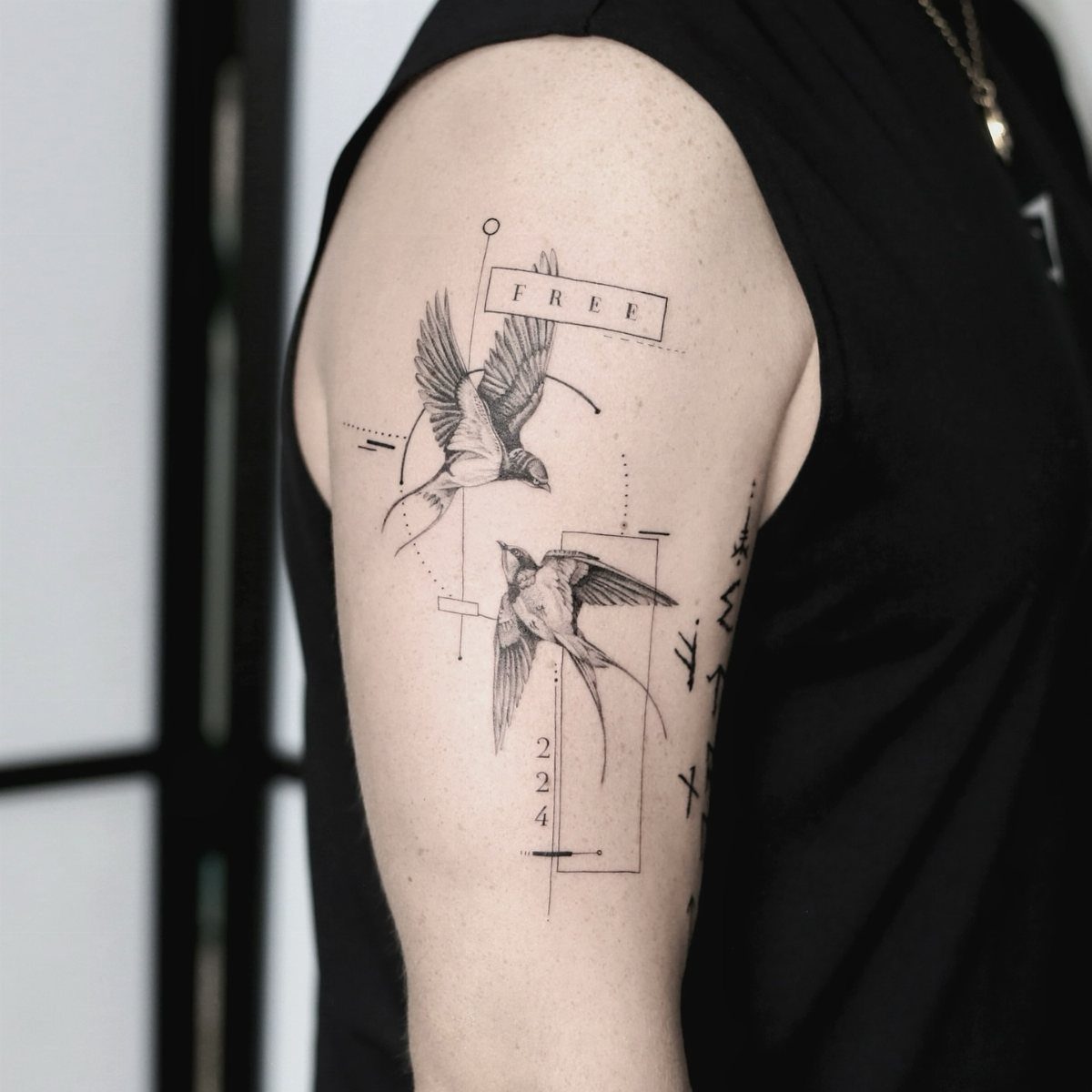 Two swallow bird tattoos with geometric lines and text on an upper arm.