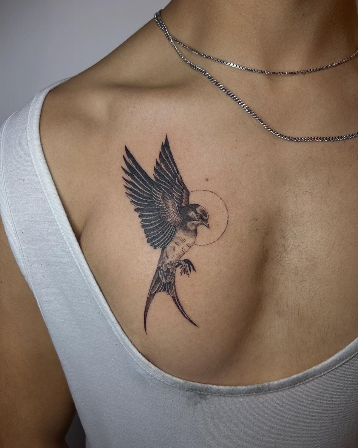 Swallow bird tattoo in flight on a person's upper chest with silver chains.