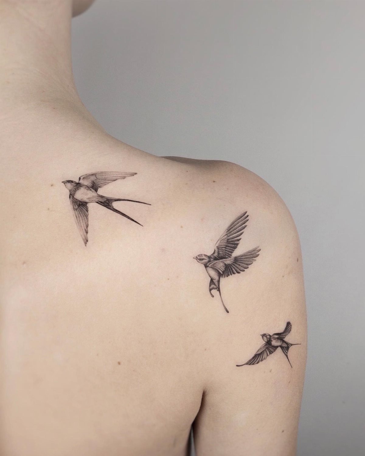 Three black ink swallow bird tattoos in flight on a person's shoulder.