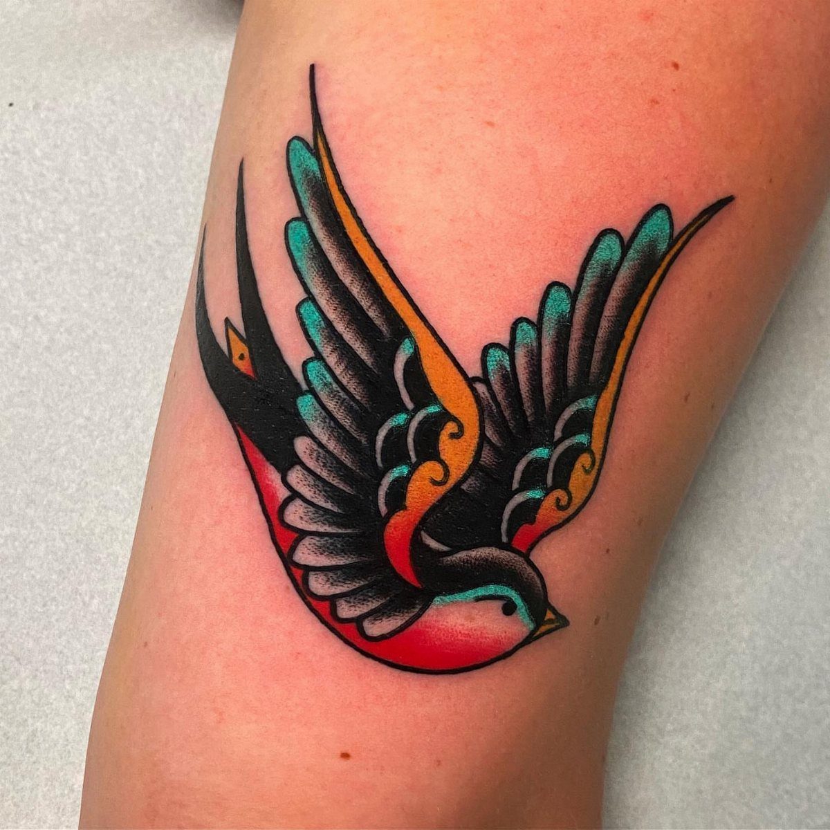 Traditional swallow bird tattoo with red, teal, and orange colors on skin.