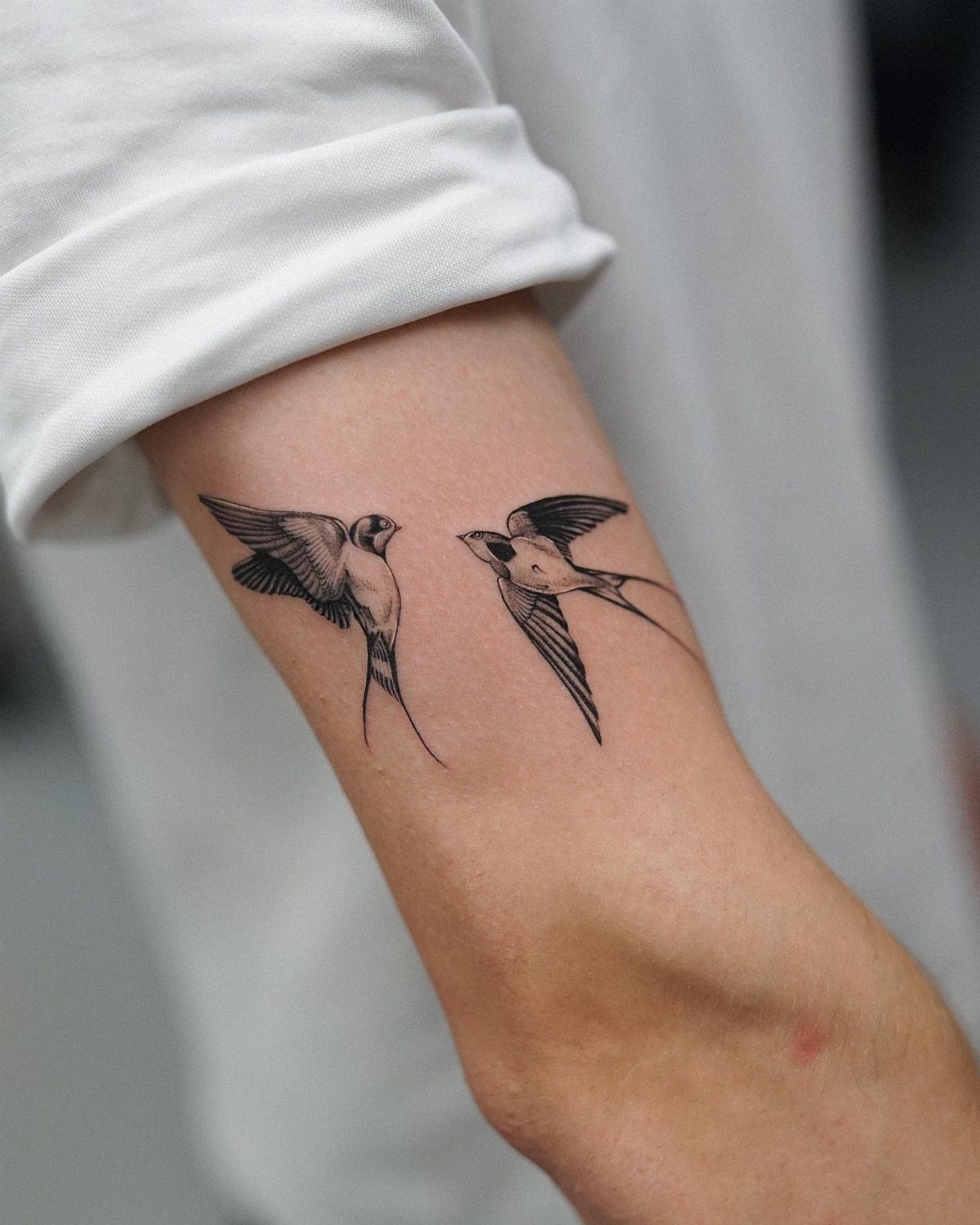 Two swallow bird tattoos in flight facing each other on a forearm