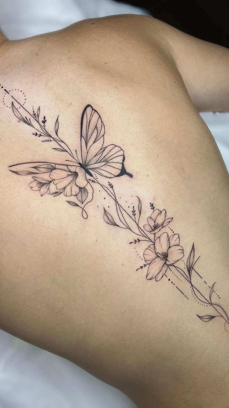 Butterfly and flower tattoo in fine black lines on a person's upper back.