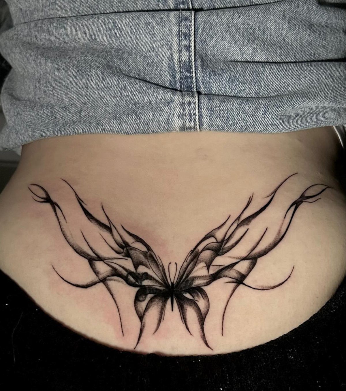 Butterfly tattoo on lower back with flowing, stylized black ink wings and shading.
