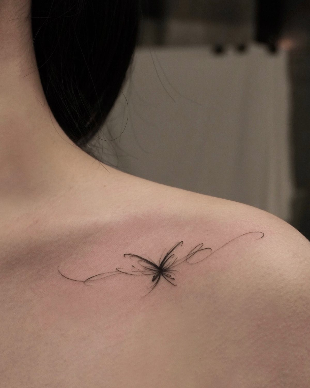 Small black ink butterfly tattoo with flowing lines on a person's upper back.