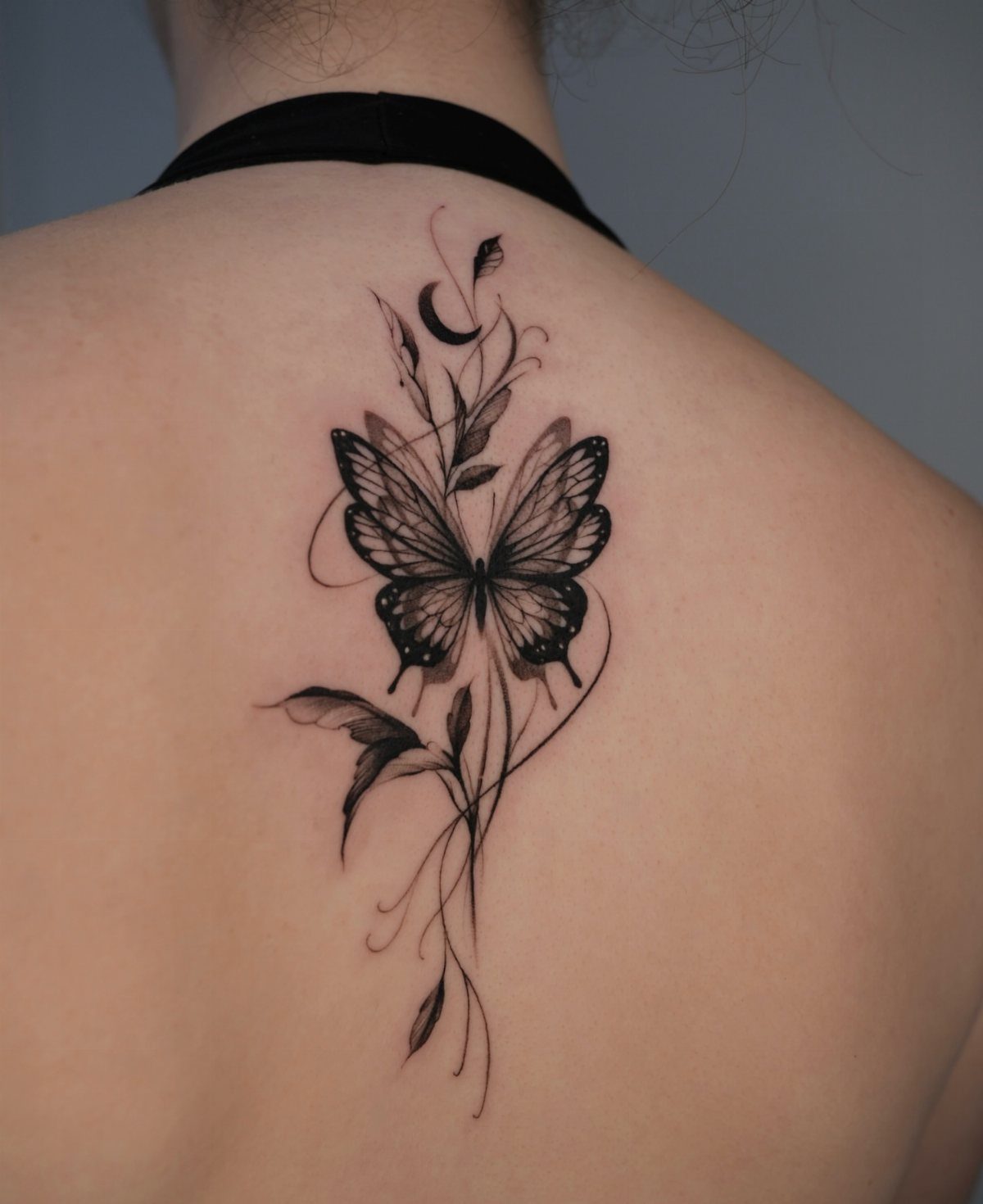 Butterfly tattoo with vines and a crescent moon centered on a person's back