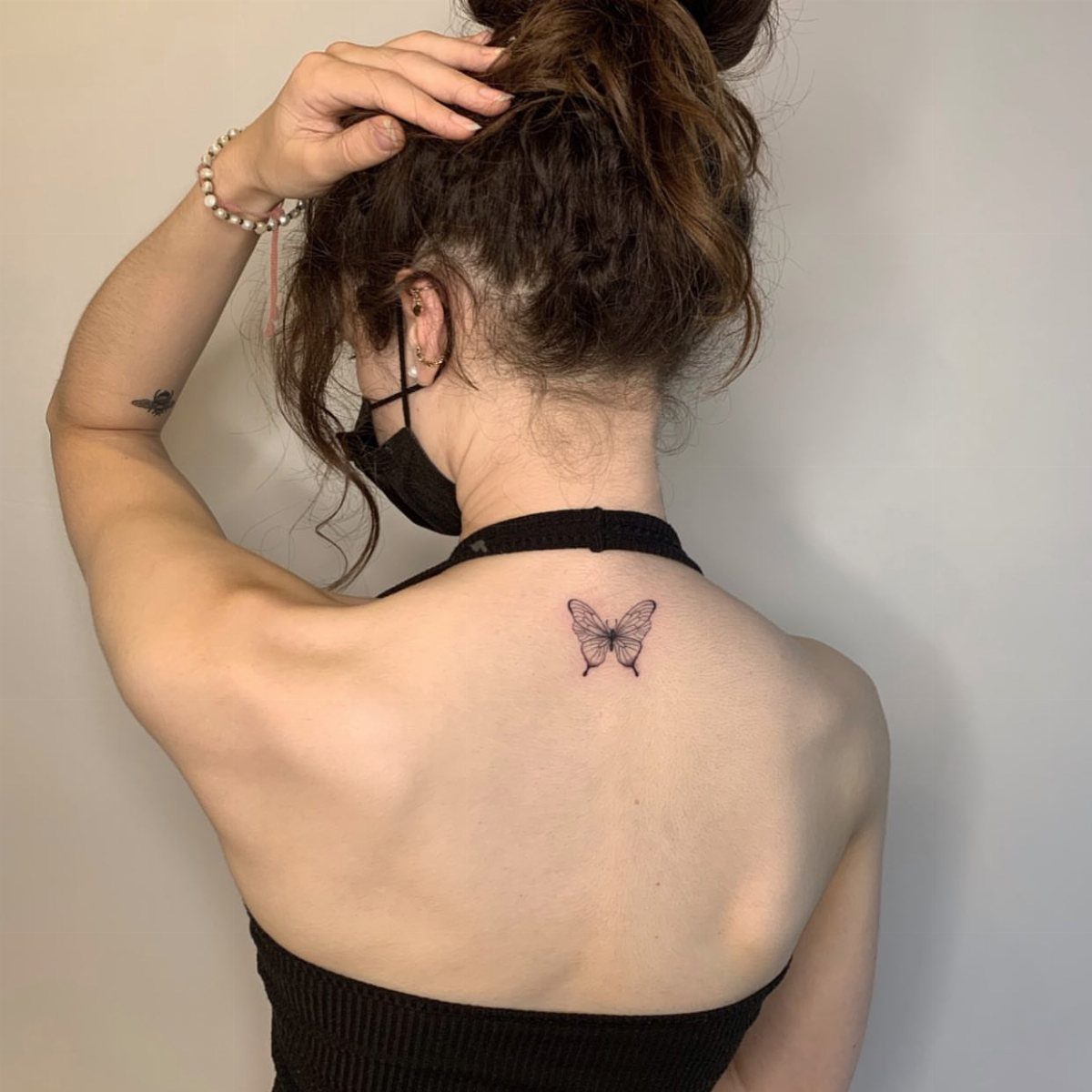 Small black butterfly tattoo centered on a woman's upper back between shoulder blades