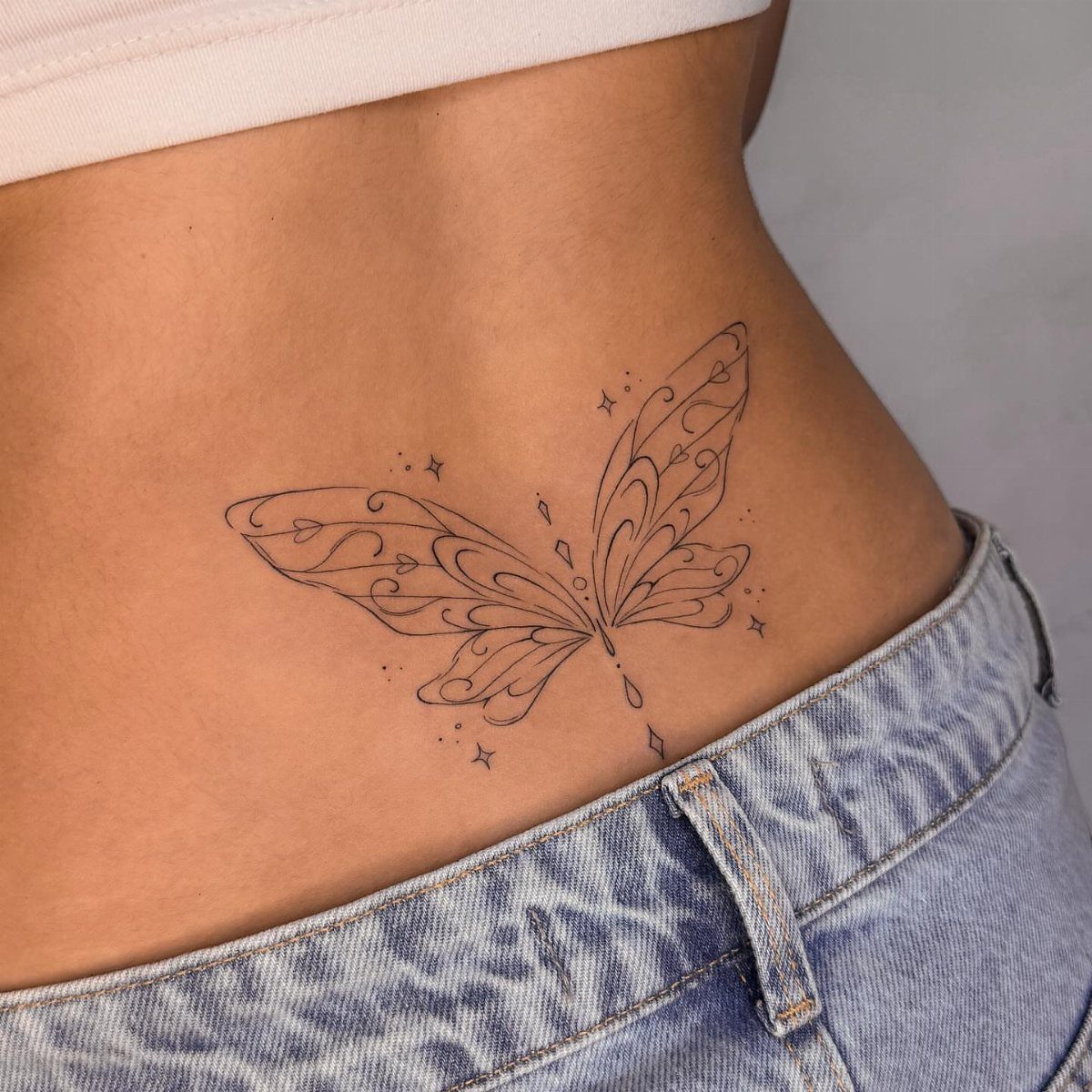 Butterfly outline tattoo with decorative swirls on a person's lower back