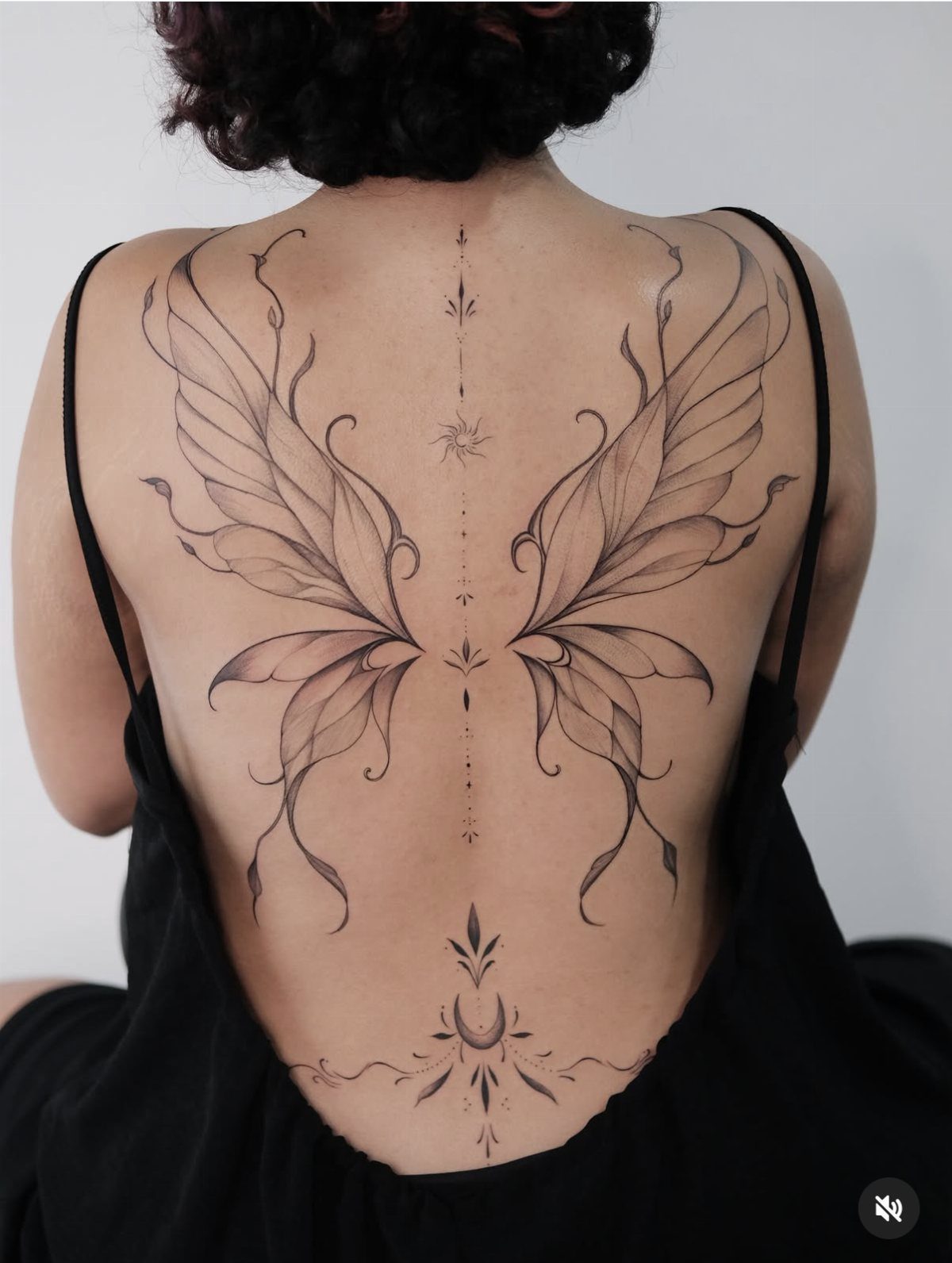 Symmetrical black ink butterfly tattoo on a person's back with spinal symbols.