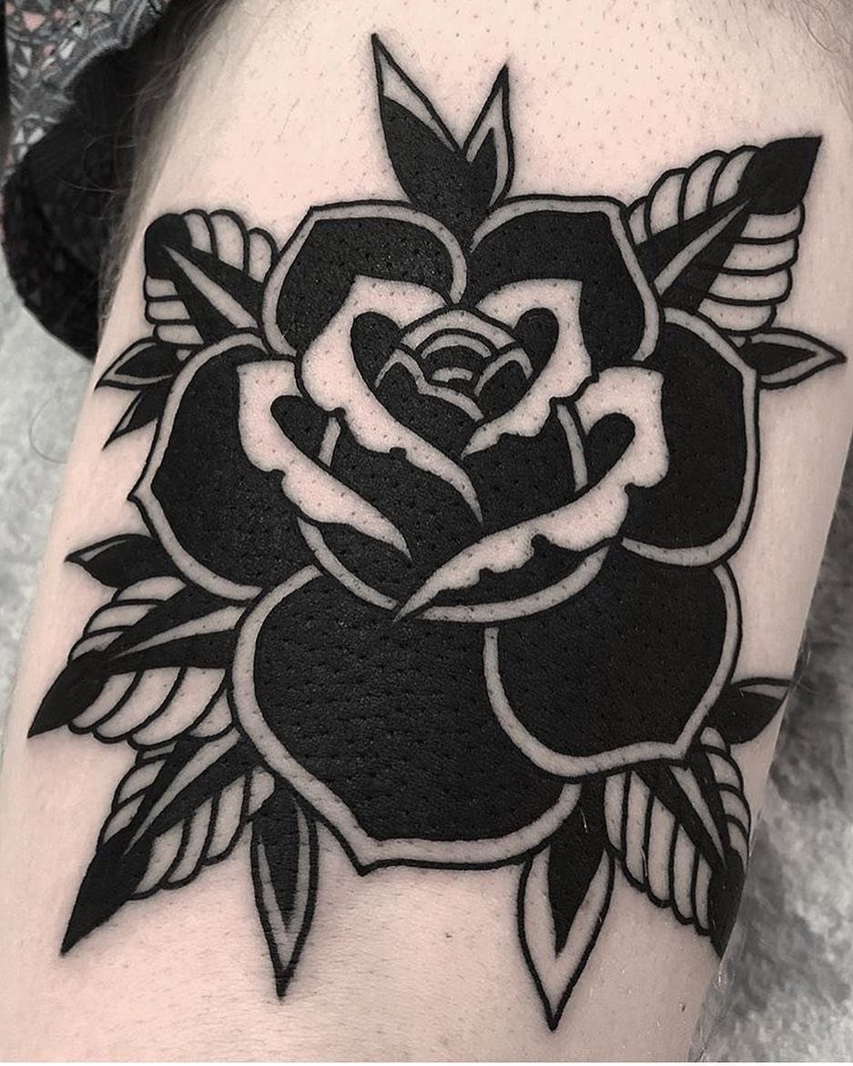 Black rose tattoo with bold outlines and leaves on a person's skin.
