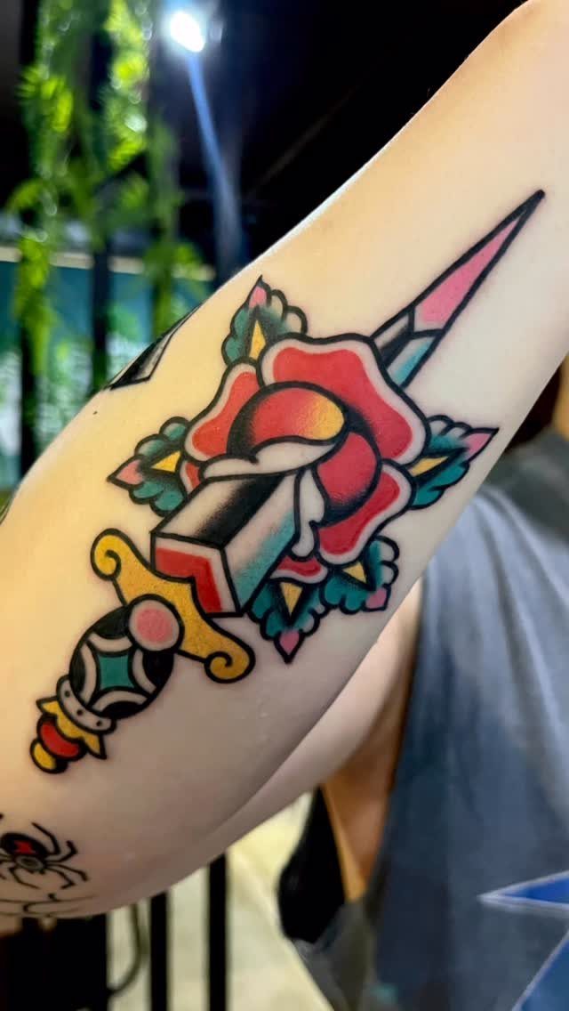 Traditional tattoo of a red rose pierced by a dagger on a forearm