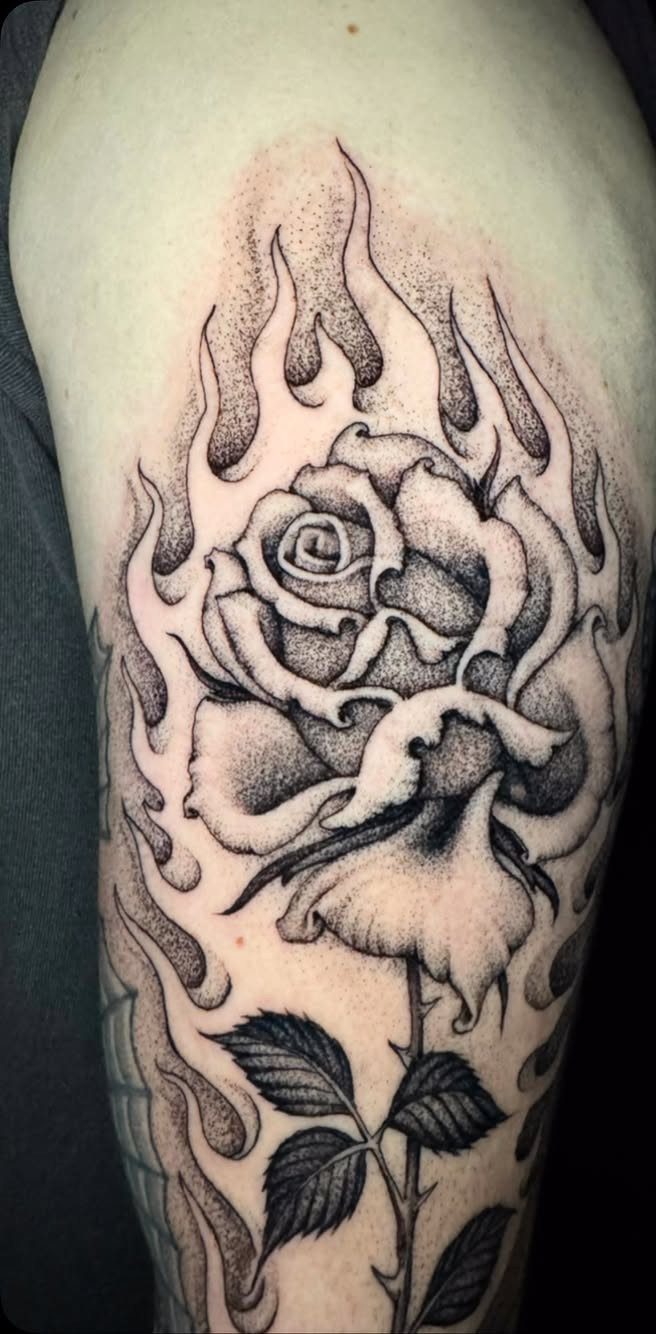 Black and grey tattoo of a rose surrounded by flames on an arm
