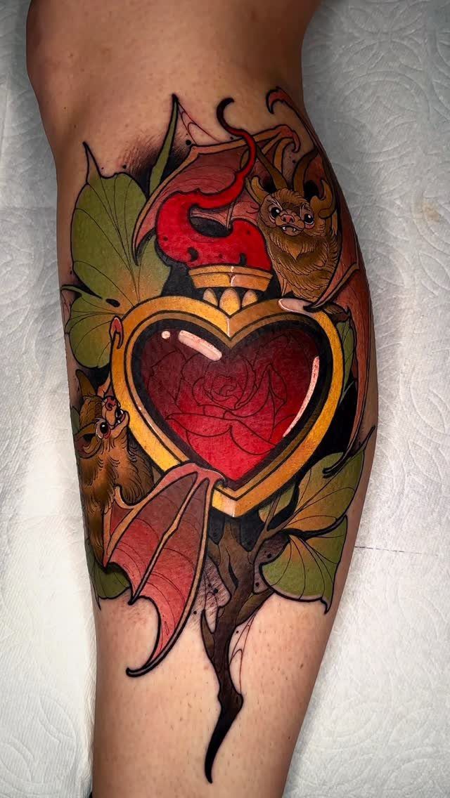 Traditional tattoo of a red rose inside a gold heart with bats and leaves