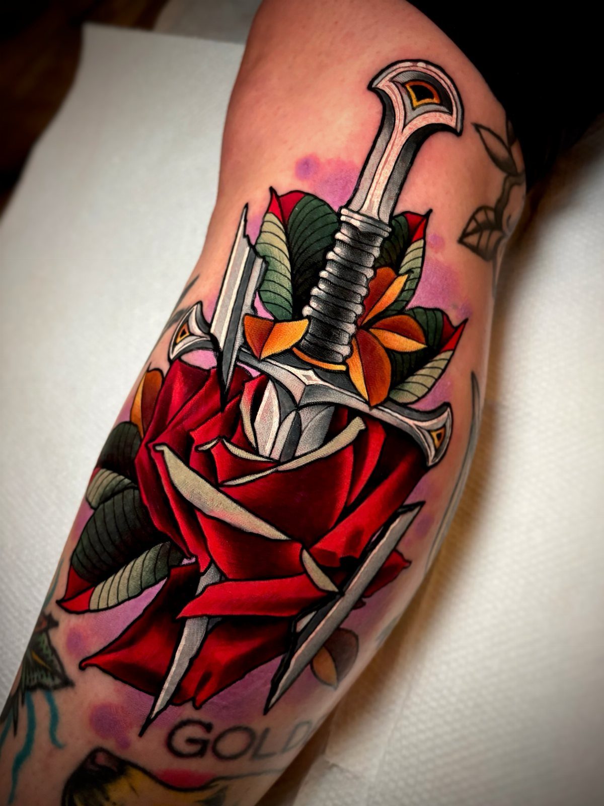 Traditional tattoo of a silver sword piercing a vibrant red rose on an arm.