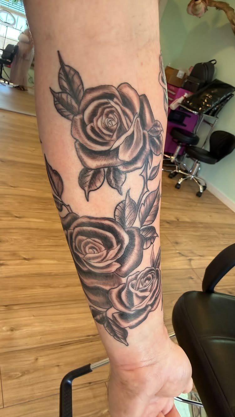 Black and grey rose tattoos with leaves on a person's forearm