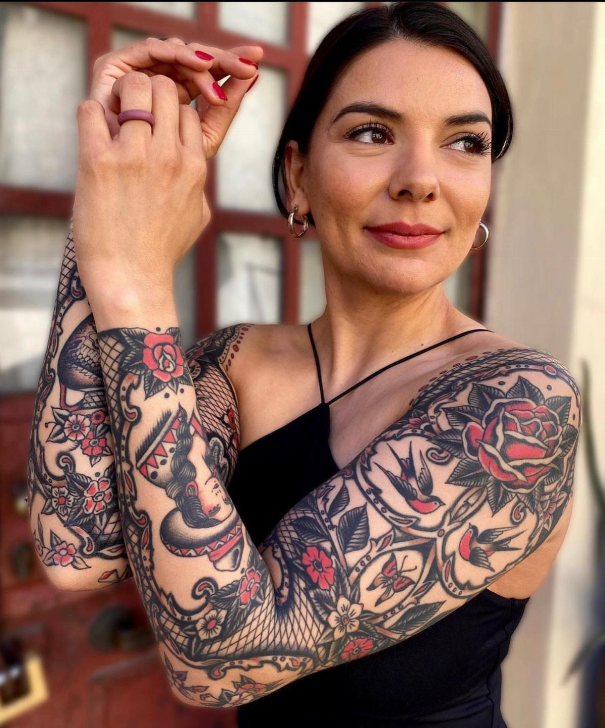 Woman with a traditional tattoo sleeve featuring red roses and swallows on her arm.