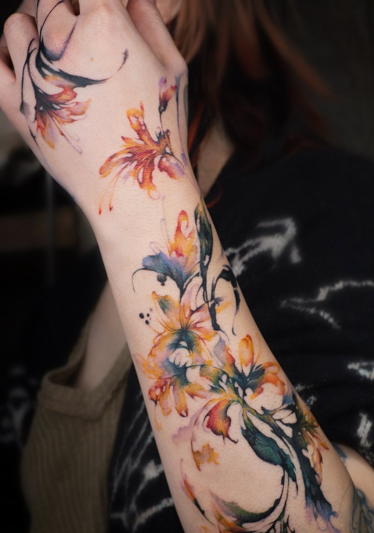 Watercolor floral tattoo with orange and blue petals on a person's forearm