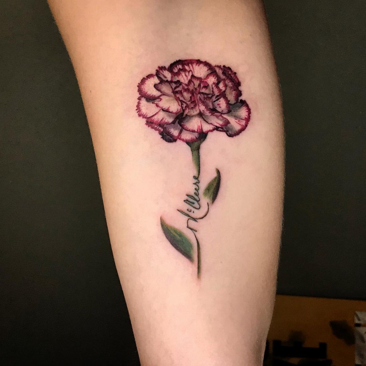 Pink and red carnation tattoo with a name integrated into the green stem.
