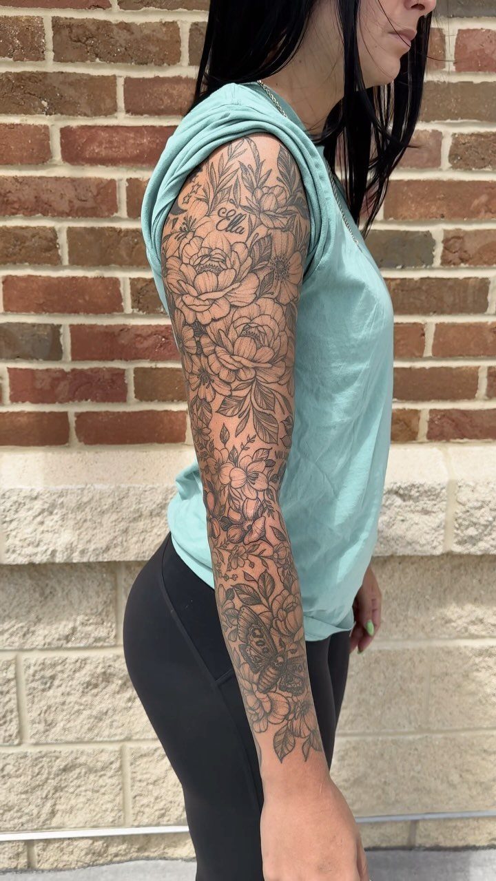 Floral sleeve tattoo on a woman's arm featuring detailed black ink roses and leaves.