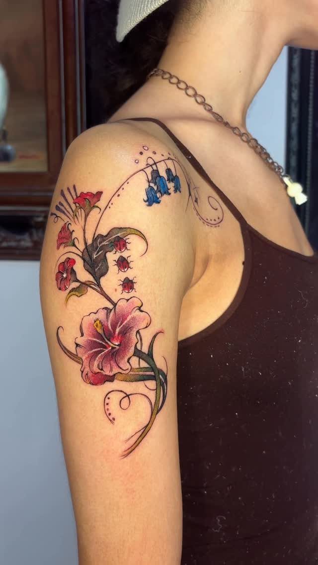 Colorful floral tattoo on a woman's shoulder featuring a large pink hibiscus flower.
