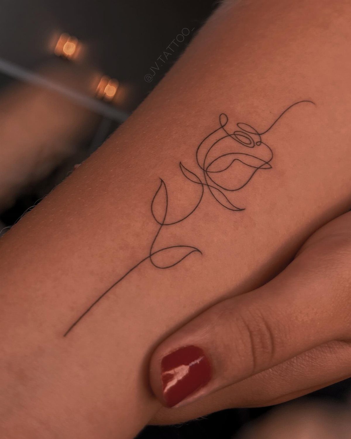 Linework rose tattoo on a forearm with a single stem and leaf.