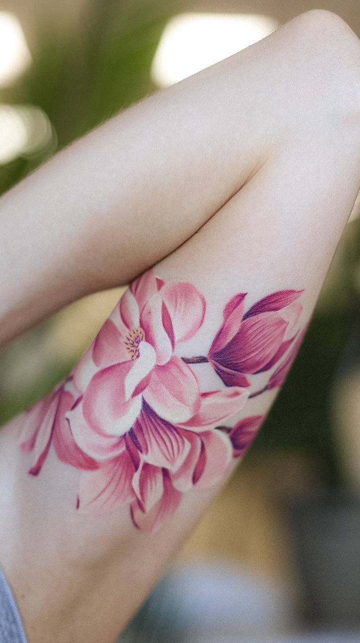 Pink and white magnolia flower tattoo on a person's upper arm.