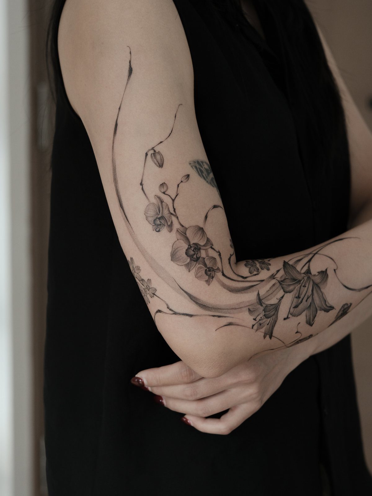 Orchid flower tattoo with flowing vines on a person's forearm and upper arm.