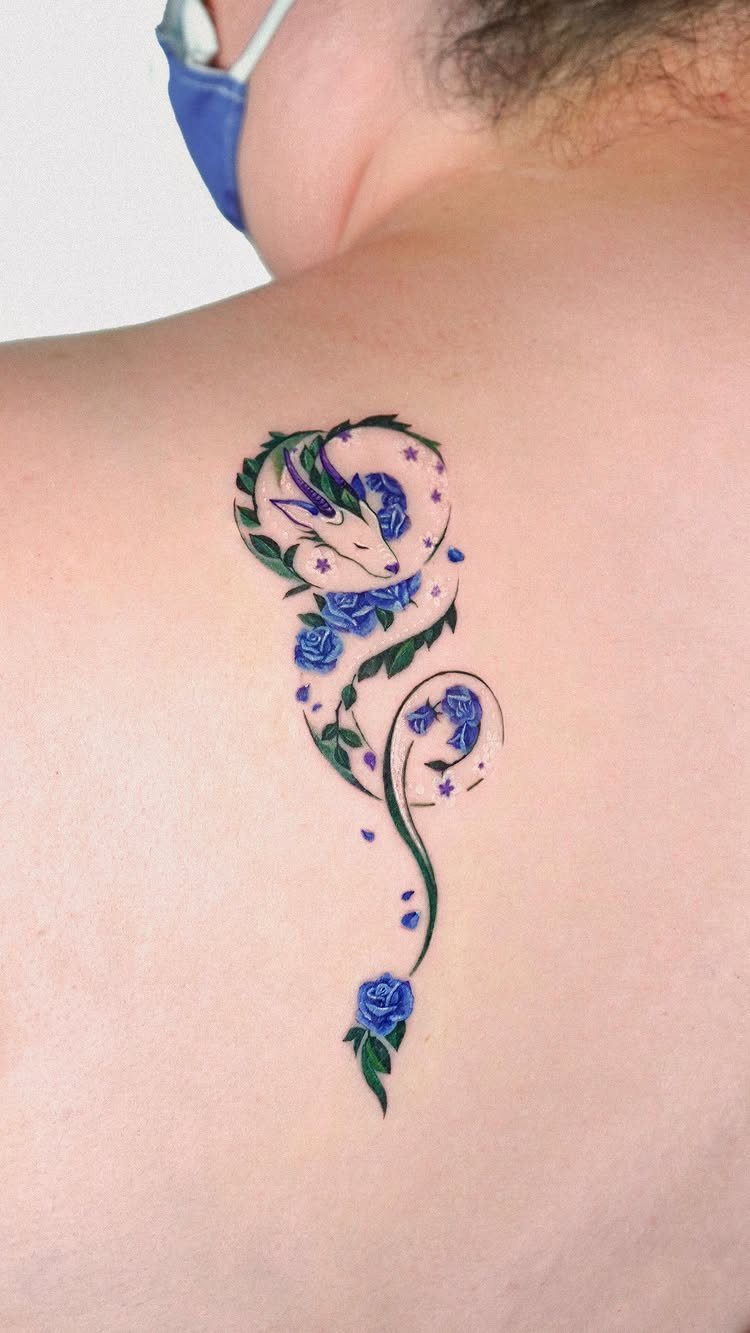 White dragon tattoo with blue roses and green leaves on a person's back