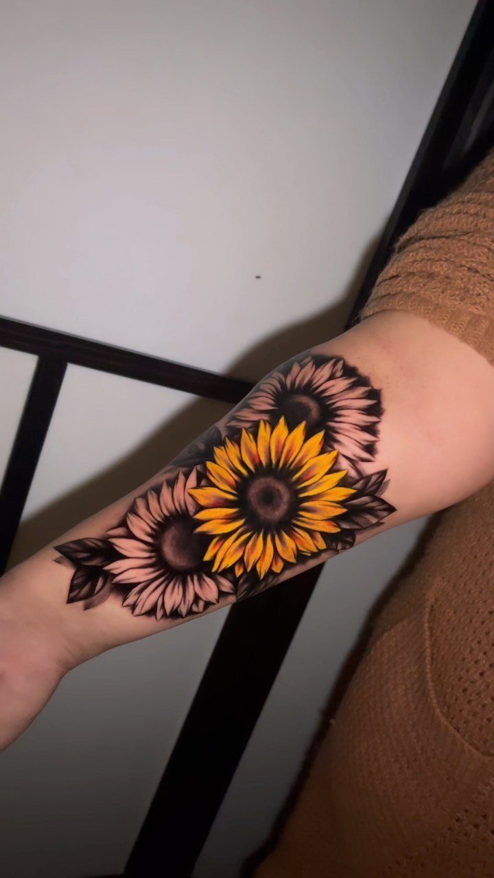 Sunflower tattoos on a forearm featuring one bright yellow and two shaded flowers.