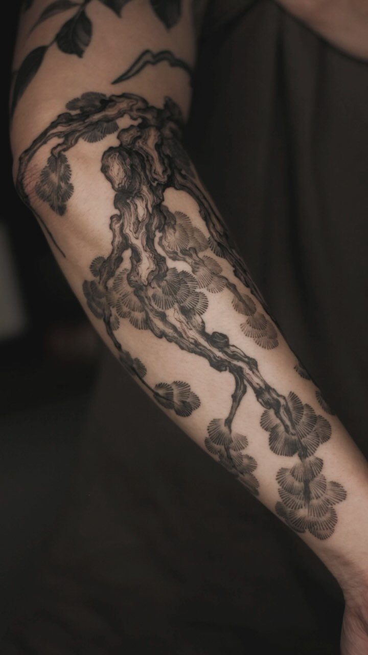 Detailed black ink floral branch tattoo extending down a person's arm