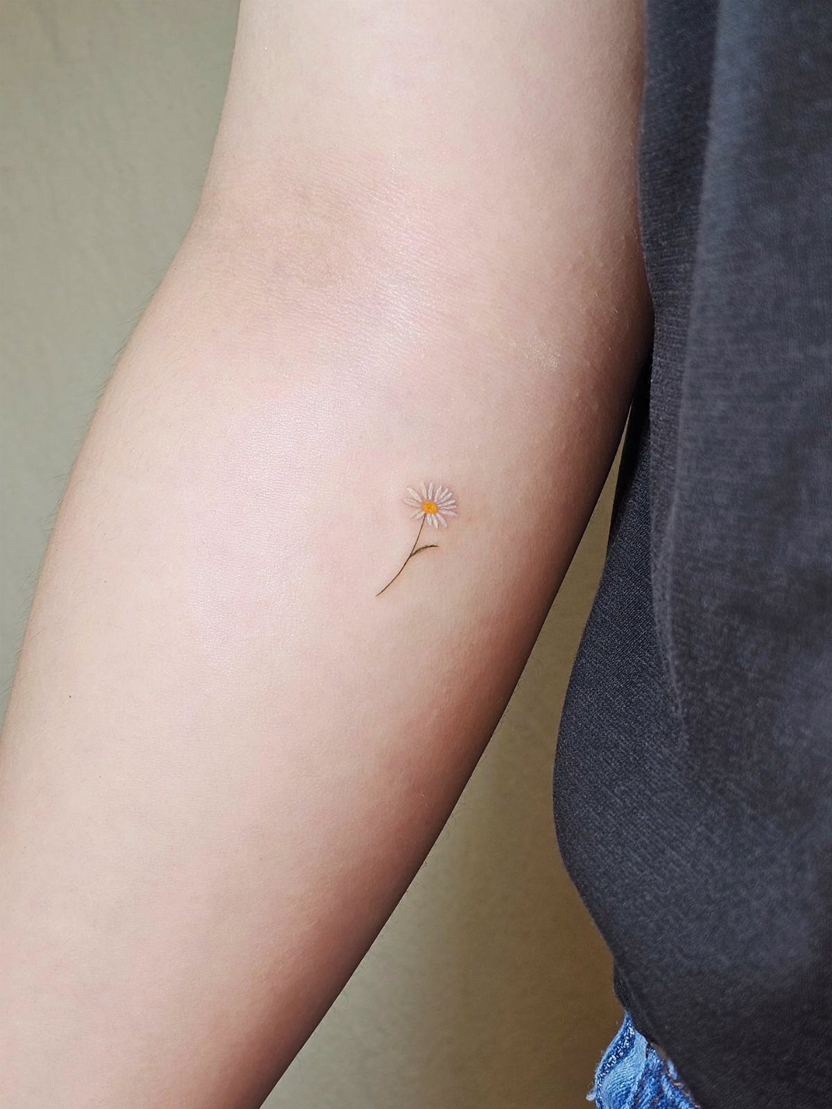 Small white daisy tattoo with a yellow center on a person's inner forearm