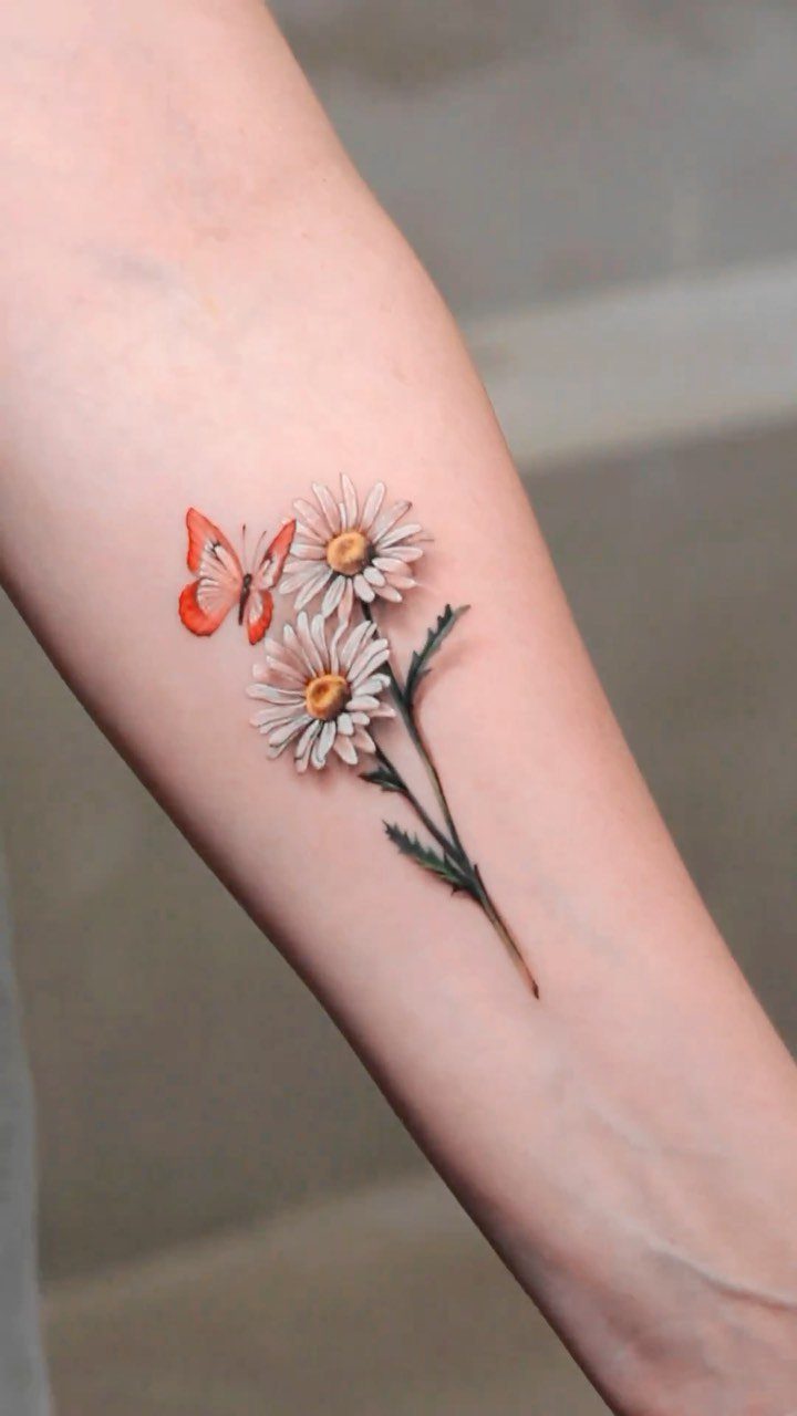 Two white daisy tattoos with an orange butterfly on a person's forearm