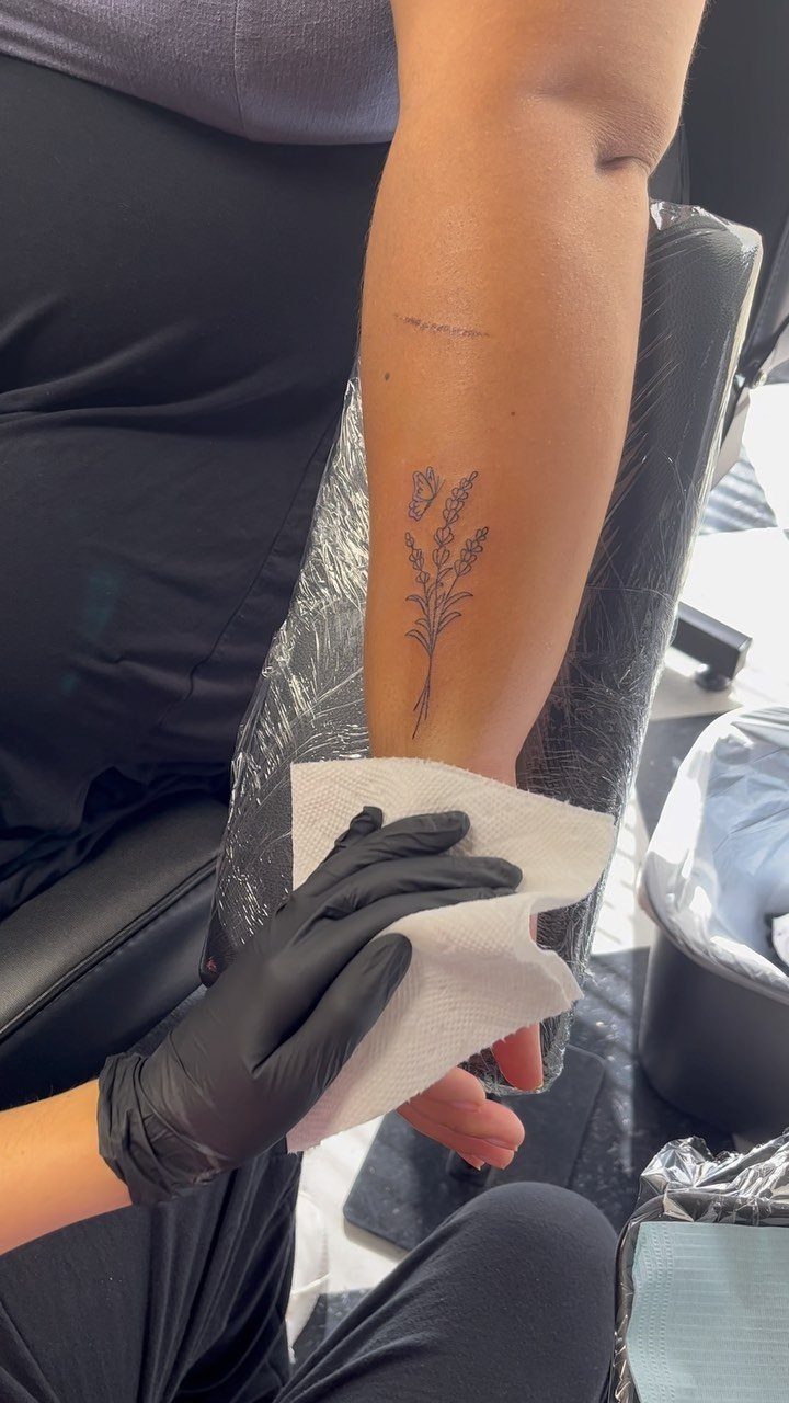Lavender sprig tattoo on a person's forearm being cleaned with a paper towel