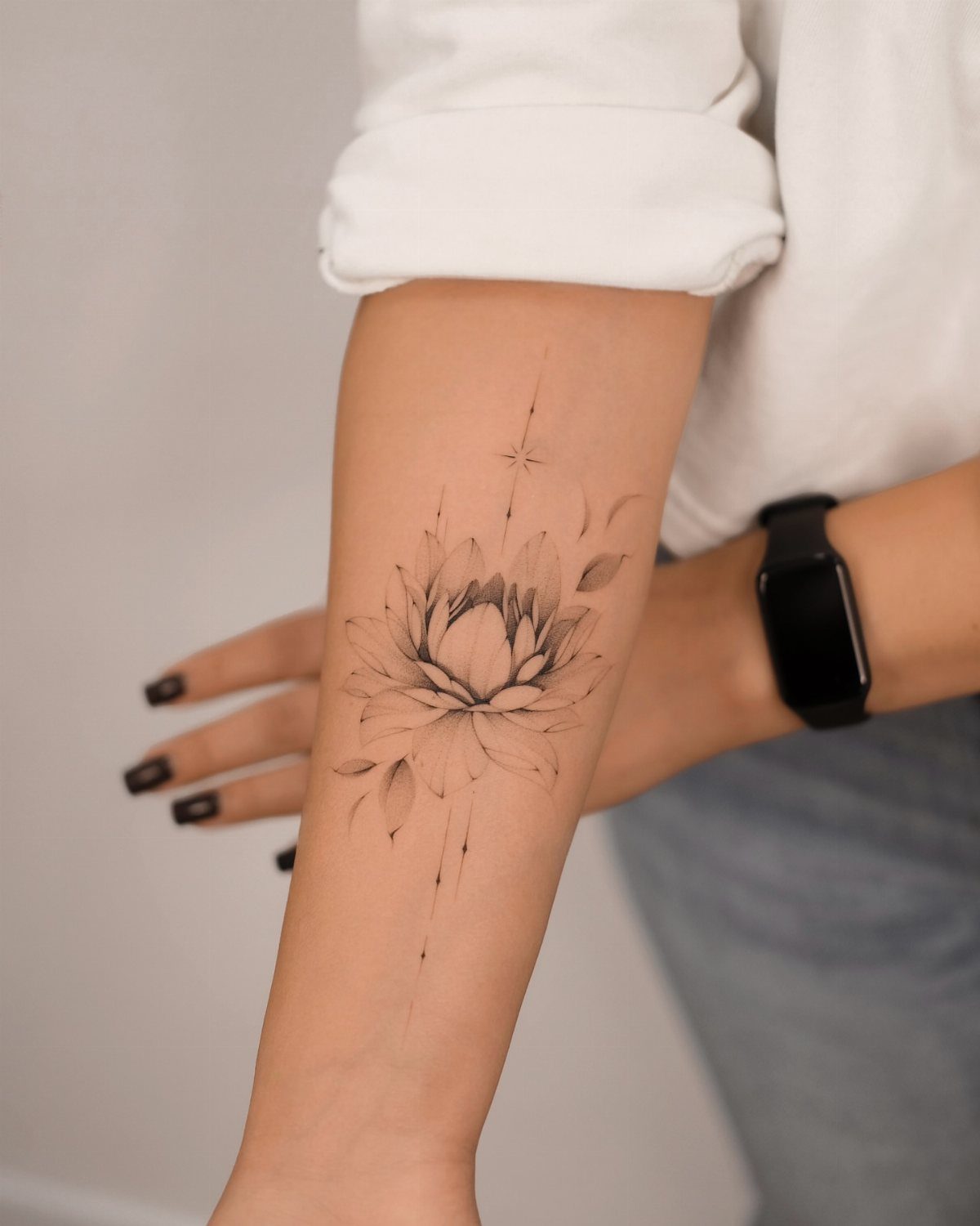 Lotus flower tattoo with fine lines and a star on a person's forearm.