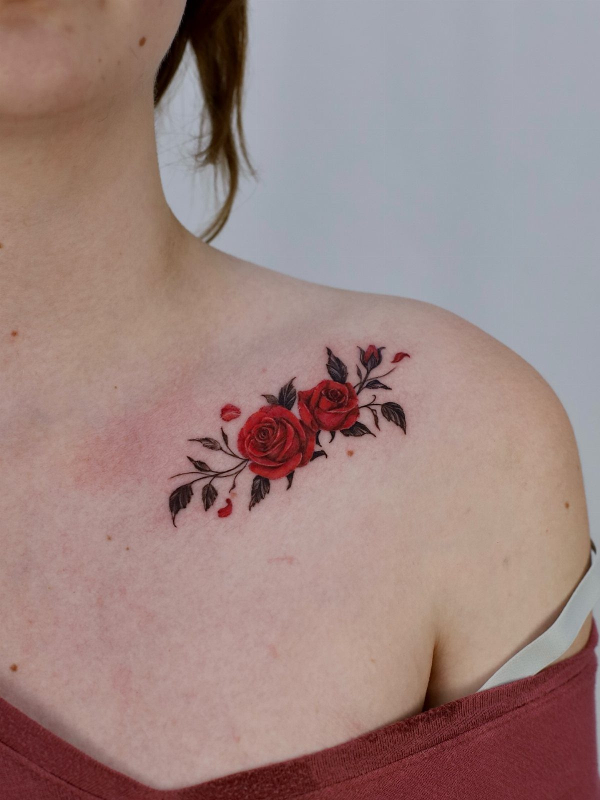 Three red rose tattoos with black leaves on a person's shoulder