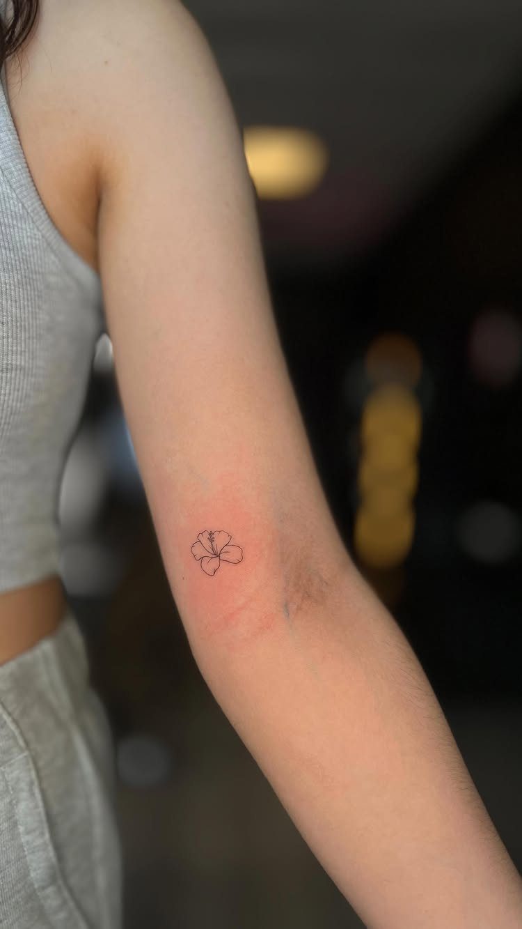 Small minimalistic black ink flower tattoo on a person's inner forearm